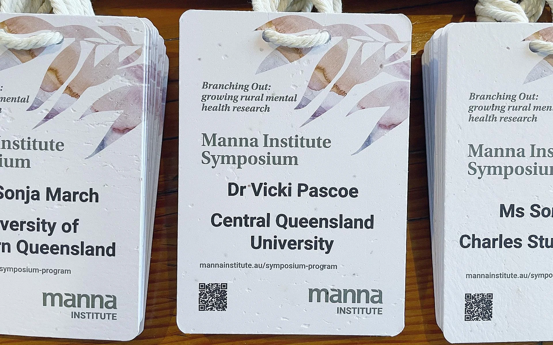 A6 seed paper conference badges for a research symposium, with the event title, name, organisation and a QR code