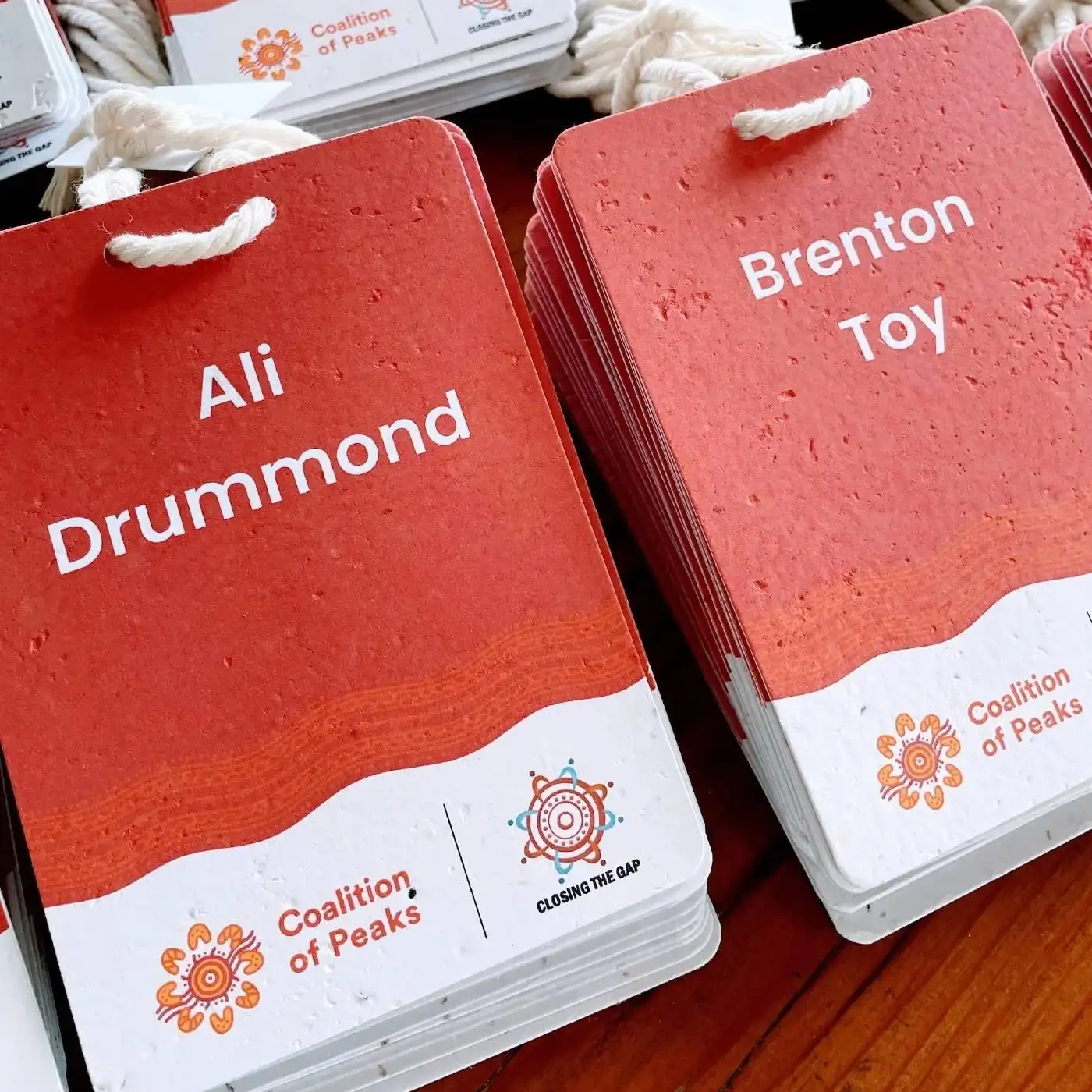 Red seed paper conference name badges with large, bold, centred names, stacked on a table